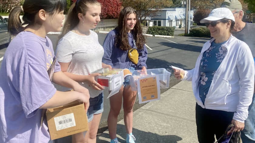 Gig Harbor High School Chinese language students (from left) Anna Daetwiler, Kaitlyn Stefanski and Mia Morente speak to passers-by to raise awareness of possible cuts in the program on Sunday, April 24, 2022, in downtown Gig Harbor.