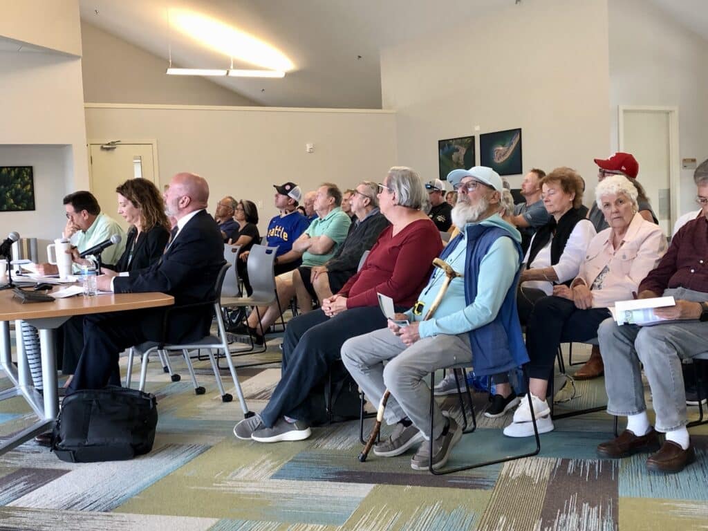 A crowd of golfers sits behind, from left, National Golf Foundation consultant Richard Singer, PenMet Executive Director Ally Bujacich and attorney Mark Roberts.