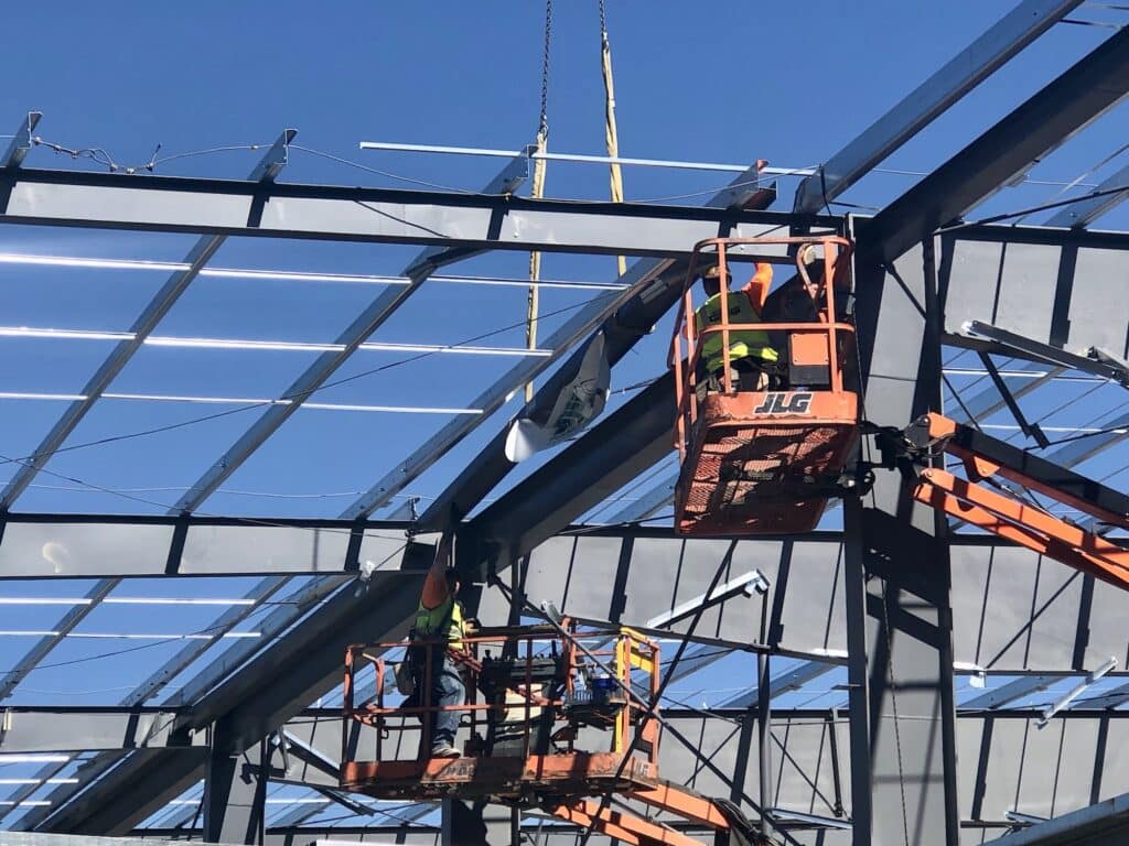 Workers on scissor lift trucks bolt the beam into place.